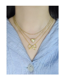 Detailed view of layered gold necklaces with polished heart and hollow bow pendants