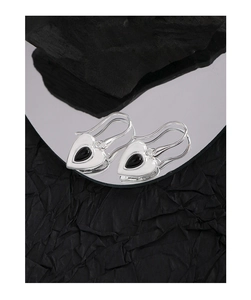 Macro detail of heart-shaped silver earrings with black agate teardrop on a mirror
