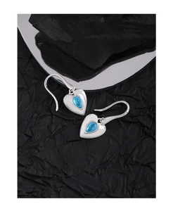Macro view of heart-shaped silver earrings with teardrop blue crystal on dark texture