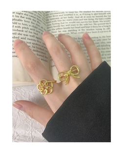 Detail of elegant hollow bow and floral open rings in gold finish on a model's hand