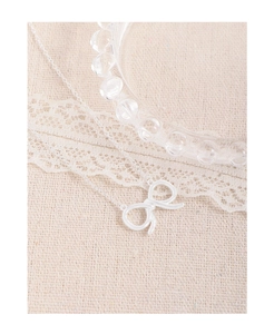 Detail shot of a silver bow necklace with streamlined design on a beige linen background