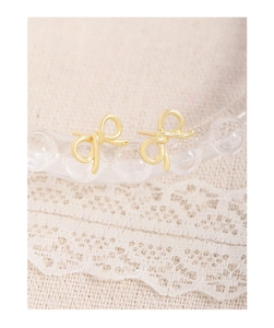 Macro shot of minimalist gold bow earrings with polished finish on a lace background