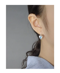 Close-up of heart-shaped silver earrings with blue pear-cut gemstone worn by a model
