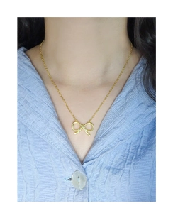 Detail of elegant gold hollow bow pendant necklace on model with blue striped shirt