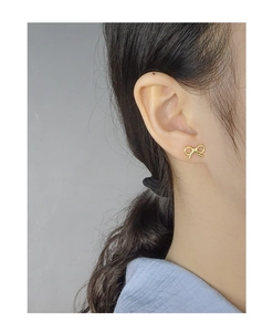 Close-up of elegant gold bow stud earrings worn on ear featuring a polished finish