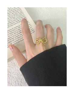 Detailed view of a gold hollow bow ring on a textured white surface with a book