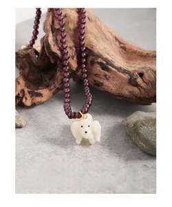 Detail of beaded garnet necklace with a cute white poodle pendant on rustic branch