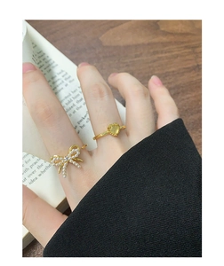 Close-up of gold bow ring with pearls and heart gemstone ring on a finger