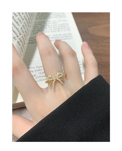 Detailed close-up of a golden bow ring with white pearls worn on a finger in elegant lighting
