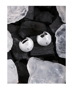 Macro shot of silver ball hoop earrings featuring a brushed matte texture and unique cut detail