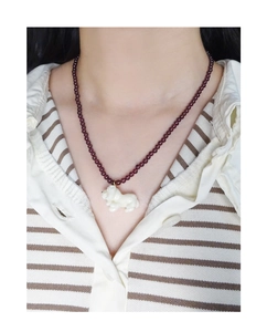 Detail view of purple garnet bead necklace with a white carved puppy pendant on a neck