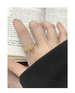 Detail of a gold bow ring with micro-pearls and zircon, worn over a vintage book background
