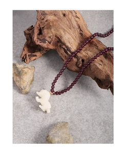 Macro shot of 925 silver necklace with red garnet beads and white puppy pendant on wood