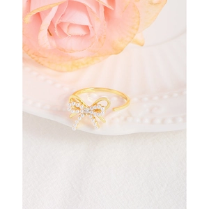 Elegant gold bow ring with pearls and square stone on a romantic floral background