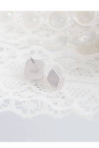 Macro detail of S925 sterling silver square agate stud earrings on white lace fabric