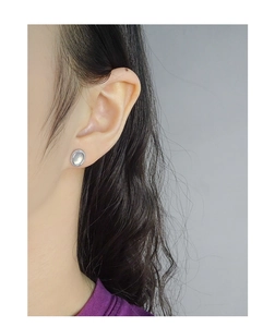 Detail of oval silver stud earring with milgrain edge and cat-eye stone on ear