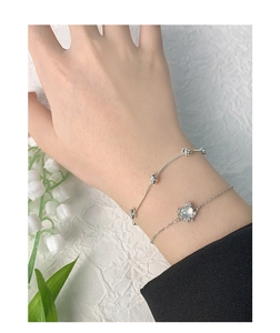 Détail d'un bracelet en argent avec agate cœur et jonc perlé porté avec muguet élégant