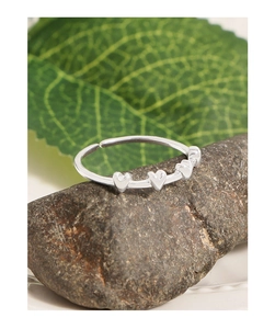 Macro detail of silver S925 heart ring on textured stone with green leaf background
