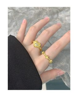 Detailed view of two gold-plated rings with heart and clover designs on a model hand