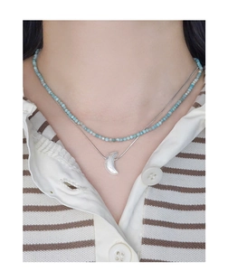 Detail of layered necklace featuring light blue stone beads and a silver crescent moon pendant