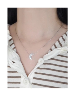 Detailed view of a silver crescent moon pendant on a delicate chain worn on neck
