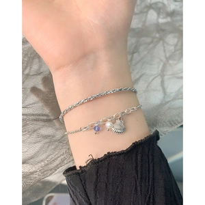 Silver double-layer bracelet with shell pendant, pearl, and bead on a mesh background