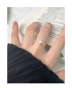 Close-up of a silver bow ring on a finger with a book background and minimalist aesthetic