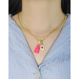 Double-layered gold necklace with pink gummy bear and sparkling heart pendant on a woman