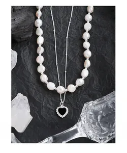Detail of a double-layer necklace with baroque pearls and a black heart pendant