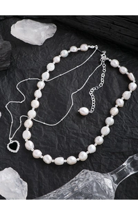 Close-up of double-layer necklace with baroque pearls and black heart pendant on dark textured background