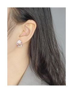 Detailed view of a silver flower earring with pink zircons worn on a model ear