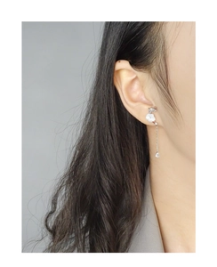 Detail of S925 silver dangling earring with white shell flower and teardrop zircon on model