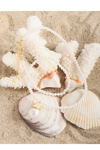 Detail of pearl necklace with large pearl pendant on a beach and coral background