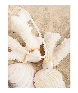 Close-up of pearl necklace with gold shell pendant on coral and sand background