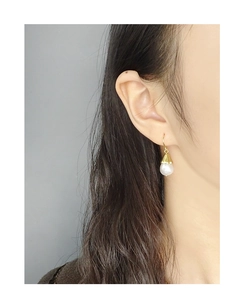 Detail of elegant gold flower petal hook earring with round white pearl on ear