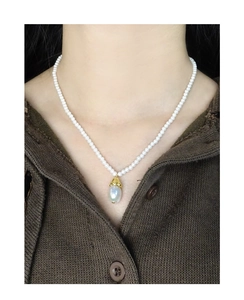 Detailed close-up of a vintage pearl necklace with a teardrop pendant on a brown sweater