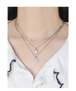 Close-up of triple-layered silver necklace featuring pink heart gemstone and white enamel charm