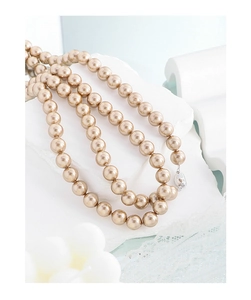 Close-up of multilayer champagne gold pearl necklace with silver clasp on white stone