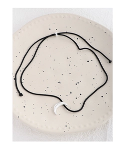 Detailed view of silver crescent moon pendant with black cord on beige ceramic tray