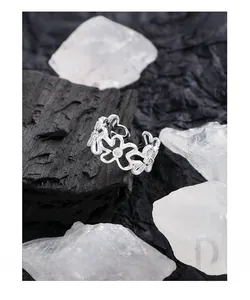 Makroaufnahme von Silberring mit hohlen Blumen und Zirkonia auf Kohle und Steinen