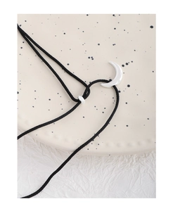 Macro detail of silver moon pendant on black cord over a textured ceramic dish