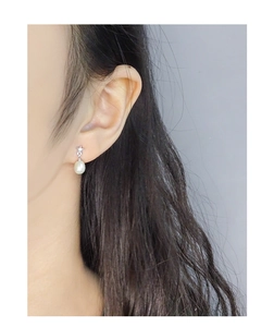 Detail of star-shaped stud earring with a white pearl drop worn on a model's ear