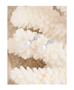 Detailed shot of star-shaped silver pearl earrings on a clean beach-style background