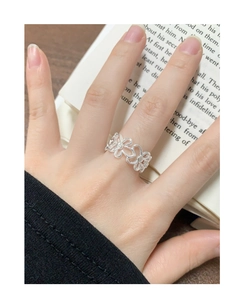 Detail eines silbernen hohlen Blumenrings mit Zirkonia am Finger vor Buchhintergrund
