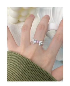 Gros plan d'une bague nœud en argent S925 avec zircon rose sur une manche tricotée