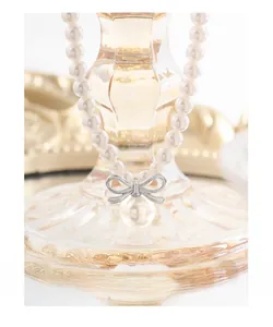 Detail of high-luster pearl necklace with silver bow pendant on a glass base