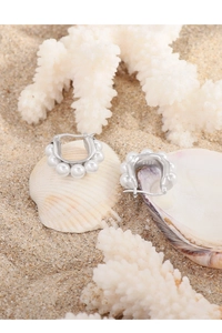 Detail of S925 silver U-shaped earrings with pearls on a beach seashell background