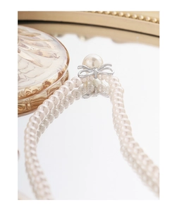 Macro detail of S925 silver bow pendant and white pearls on a reflective mirror surface