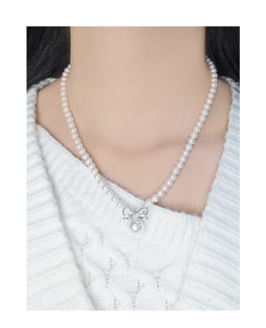 Detail of silver bow pendant and elegant white pearls worn on a white knit sweater