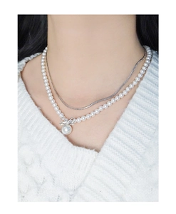 Detail of layered S925 silver bow necklace with elegant pearls on a white sweater